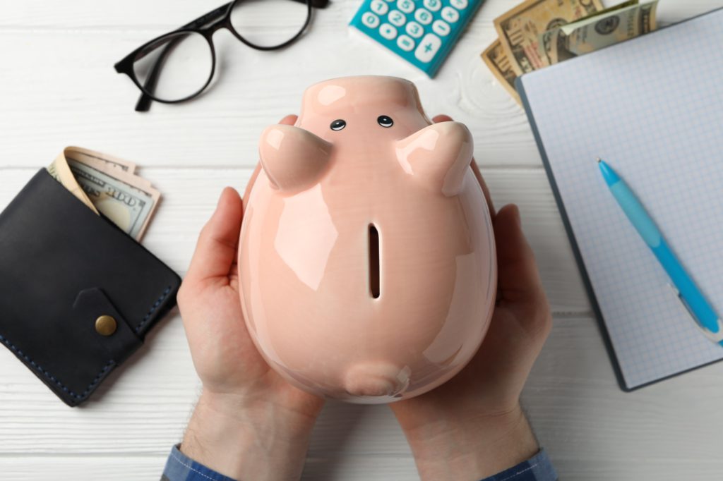 Pension concept. Male hands hold Piggy bank on white wooden background, top view